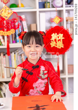 Little Asian Girl Writing Chinese Calligraphy Fai Chun for New Year Decoration,The text on the pendant hanging at the back reads: "Happy New Year." 141709269
