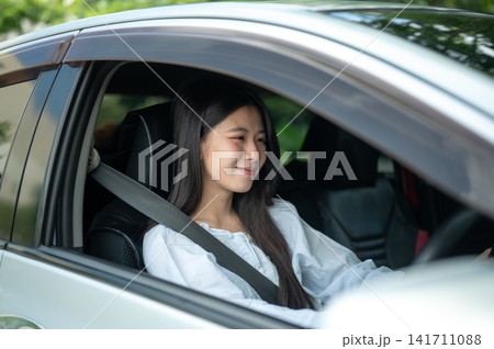 Young Asian woman seated comfortably while driving a car wearing seatbelt behind the steering wheel. 141711088