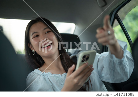 Young Asian woman giving a direction to driver while traveling in the back seat of a taxi cab car. Young Asian woman giving a direction to driver while traveling in the back seat of a taxi cab car. 141711099