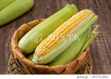 fresh green sweet corn with husks and cooked corn segments on plate fresh green sweet corn with husks and cooked corn segments on plate 141711361