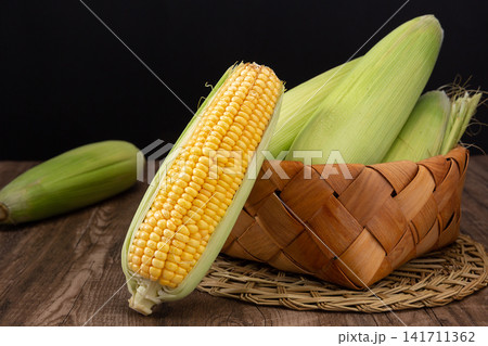 fresh green sweet corn with husks and cooked corn segments on plate fresh green sweet corn with husks and cooked corn segments on plate 141711362