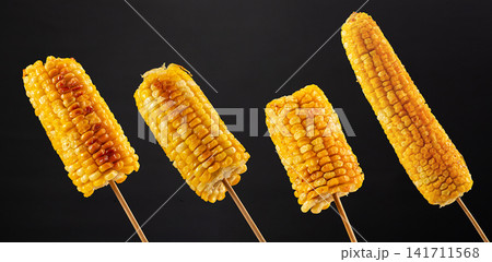 grilled sweet corn on wooden skewers served on a white plate grilled sweet corn on wooden skewers served on a white plate 141711568