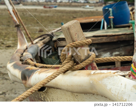 Close up of old wooden fishing boat bow with thick rope tied around wooden post Close up of old wooden fishing boat bow with thick rope tied around wooden post 141712206