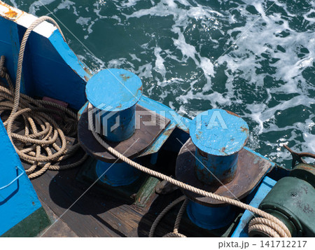 Blue mooring bitts with thick ropes on a ship deck over bubbling ocean sea water background 141712217