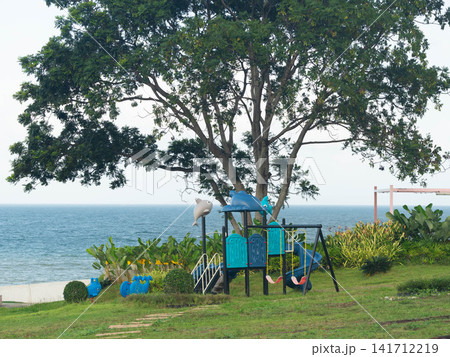 Outdoor playground under a large spreading tree near the lake shore in daylight Outdoor playground under a large spreading tree near the lake shore in daylight 141712219