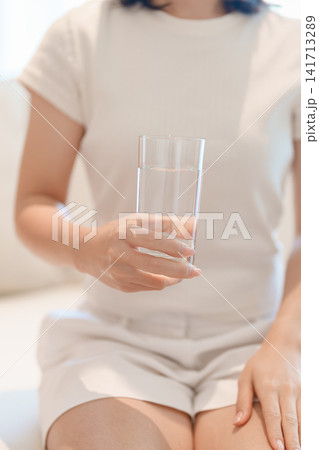 Healthy woman hold glass of clean mineral water glass on sofa at home, female drink pure water for hydration and wellness, fresh skin care, daily routine water intake, Refreshment and lifestyle Healthy woman hold glass of clean mineral water glass on sofa at home, female drink pure water for hydration and wellness, fresh skin care, daily routine water intake, Refreshment and lifestyle 141713289