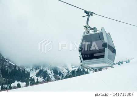 Ski gondola glides through misty atmosphere toward mountain peak Ski gondola glides through misty atmosphere toward mountain peak 141713307