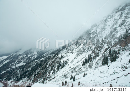 Snow blankets mountainous terrain under misty clouds 141713315