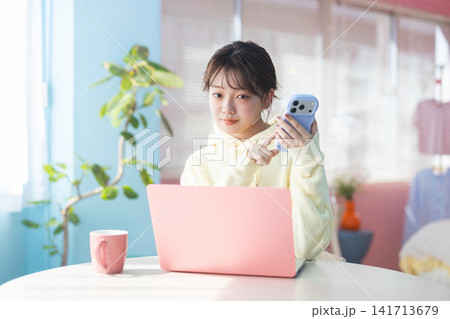 スマホを操作しながらカメラ目線で微笑む若い女性 スマホを操作しながらカメラ目線で微笑む若い女性 141713679