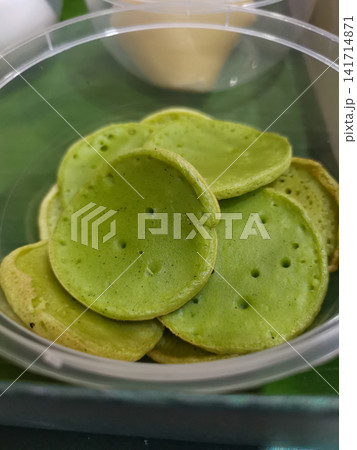 Traditional Indonesian pandan rice pancakes packed in a clear takeaway container. Authentic Southeast Asian snack suitable for restaurant, food delivery, travel, hospitality, and culinary projects. 141714871