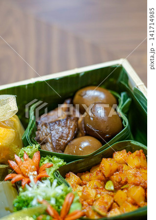 Traditional Indonesian food hamper featuring braised eggs, fried tofu, lontong and festive side dishes arranged in a bamboo basket for Ramadan, Eid, catering and family celebrations. Traditional Indonesian food hamper featuring braised eggs, fried tofu, lontong and festive side dishes arranged in a bamboo basket for Ramadan, Eid, catering and family celebrations. 141714985