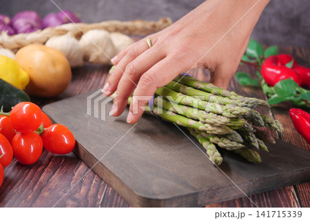Preparing fresh asparagus on a wooden cutting board Preparing fresh asparagus on a wooden cutting board 141715339