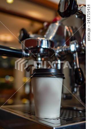 Espresso machine preparing coffee in takeaway cup with warm cafe lighting and shallow focus. Perfect for coffee shop and lifestyle concepts. Espresso machine preparing coffee in takeaway cup with warm cafe lighting and shallow focus. Perfect for coffee shop and lifestyle concepts. 141715414