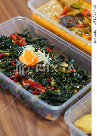 Traditional Indonesian oseng daun singkong stir fried cassava leaves with chili and spices healthy vegan vegetable dish served in plastic takeaway container Traditional Indonesian oseng daun singkong stir fried cassava leaves with chili and spices healthy vegan vegetable dish served in plastic takeaway container 141715419