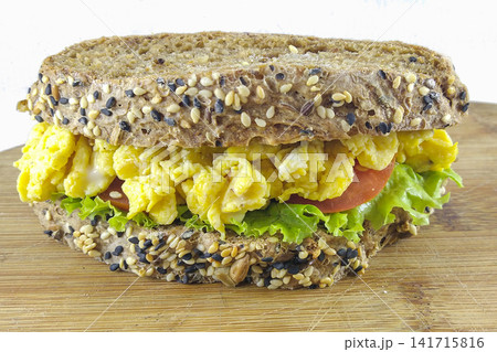 Close-up of healthy scrambled egg sandwich on whole grain seeded bread with lettuce and tomato. High protein clean eating breakfast isolated on white background. Close-up of healthy scrambled egg sandwich on whole grain seeded bread with lettuce and tomato. High protein clean eating breakfast isolated on white background. 141715816