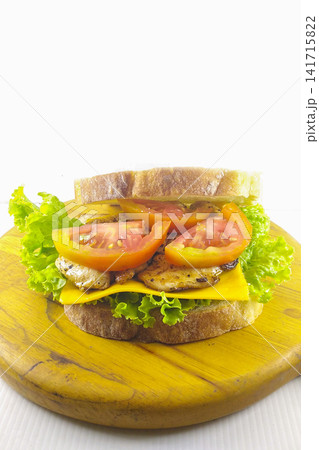 Fresh grilled chicken sandwich with cheese lettuce and tomato on wooden board healthy homemade meal isolated on white background. Fresh grilled chicken sandwich with cheese lettuce and tomato on wooden board healthy homemade meal isolated on white background. 141715822