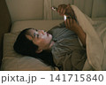 ベッドでスマホを見る若い女性 141715840