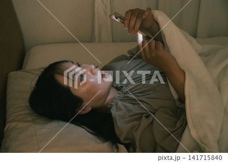 ベッドでスマホを見る若い女性 ベッドでスマホを見る若い女性 141715840