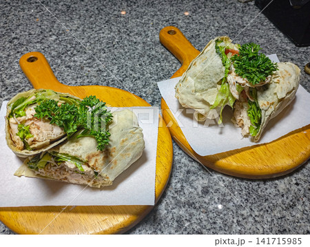 Fresh chicken tortilla wrap with lettuce and parsley served on wooden board in kitchen healthy homemade meal. Fresh chicken tortilla wrap with lettuce and parsley served on wooden board in kitchen healthy homemade meal. 141715985