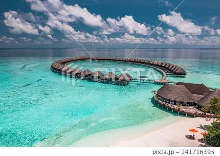 Breathtaking aerial view of circular overwater villas over turquoise lagoon Maldives luxury resort blue sea. Perfect summer vacation travel landscape paradise. Luxury honeymoon getaway scenic Breathtaking aerial view of circular overwater villas over turquoise lagoon Maldives luxury resort blue sea. Perfect summer vacation travel landscape paradise. Luxury honeymoon getaway scenic 141716395