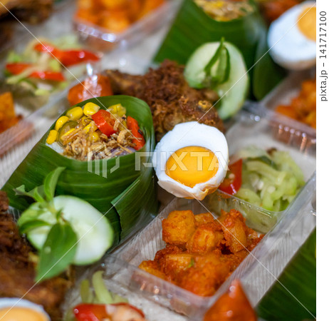 Traditional Indonesian Nasi Tempong rice boxes wrapped in banana leaf with fried chicken, boiled egg, sambal and vegetable side dishes for catering and takeaway. 141717100