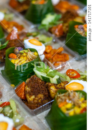 Traditional Indonesian Nasi Tempong rice boxes wrapped in banana leaf with fried chicken, boiled egg, sambal and vegetable side dishes for catering and takeaway. 141717101