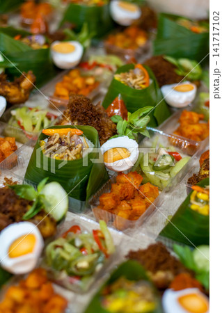 Traditional Indonesian Nasi Tempong rice boxes wrapped in banana leaf with fried chicken, boiled egg, sambal and vegetable side dishes for catering and takeaway. 141717102