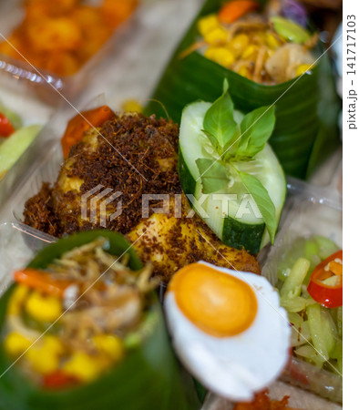 Traditional Indonesian Nasi Tempong featuring crispy Ayam Goreng Laos, salted egg, banana leaf rice, sambal and fresh vegetables. Authentic Banyuwangi culinary specialty. 141717103