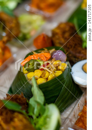 Traditional Indonesian Nasi Tempong featuring banana leaf rice, Ayam Goreng Laos, salted egg, sambal, anchovies and colorful vegetables. Authentic Banyuwangi culinary specialty. Traditional Indonesian Nasi Tempong featuring banana leaf rice, Ayam Goreng Laos, salted egg, sambal, anchovies and colorful vegetables. Authentic Banyuwangi culinary specialty. 141717105