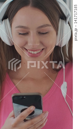 Vertical video. Young woman passenger enjoying trip at the public transport, sitting with headphones near the window in the modern tram. Vertical video. Young woman passenger enjoying trip at the public transport, sitting with headphones near the window in the modern tram. 141717185