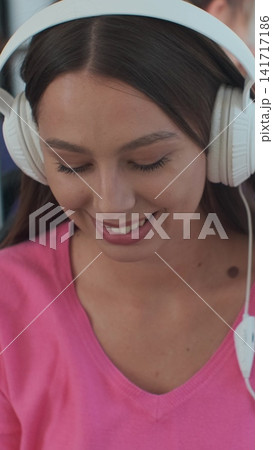 Vertical video. Portrait of a young woman passenger enjoying trip at the public transport, sitting with headphones in the modern tram. Vertical video. Portrait of a young woman passenger enjoying trip at the public transport, sitting with headphones in the modern tram. 141717186