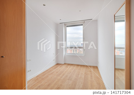 Empty bright room with light oak wooden floor, large window, white walls and tall wall mirror, creating minimalist interior with spacious modern residential feel Empty bright room with light oak wooden floor, large window, white walls and tall wall mirror, creating minimalist interior with spacious modern residential feel 141717304