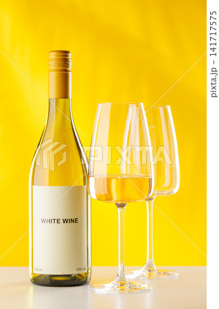 White wine bottle and glasses on yellow background elegant drink setup 141717575