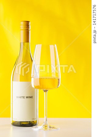 White wine bottle and glass on yellow background elegant drink setup 141717576