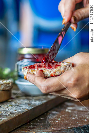 Close-up rustic breakfast scene of sourdough bread with strawberry jam, hands spreading the jam, natural light, shallow focus, and homemade styling. Close-up rustic breakfast scene of sourdough bread with strawberry jam, hands spreading the jam, natural light, shallow focus, and homemade styling. 141717630