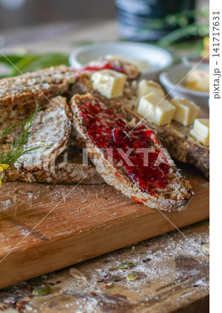 Close-up rustic food still life of sourdough bread with strawberry jam and butter on a wooden board, styled as a cozy homemade breakfast. Close-up rustic food still life of sourdough bread with strawberry jam and butter on a wooden board, styled as a cozy homemade breakfast. 141717631