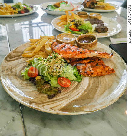 Grilled salmon with fresh salad and fries served on plate. Healthy western style meal with balanced nutrition. 141717633
