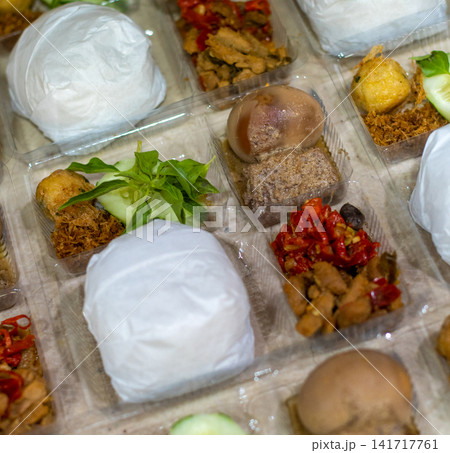 Traditional Indonesian Nasi Langgi served in takeaway meal boxes with steamed rice, beef, braised egg, sambal, cucumber, and authentic side dishes. Ideal for Southeast Asian food, catering, restaurant Traditional Indonesian Nasi Langgi served in takeaway meal boxes with steamed rice, beef, braised egg, sambal, cucumber, and authentic side dishes. Ideal for Southeast Asian food, catering, restaurant 141717761