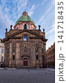 Historic Church of Saint Francis of Assisi with green Baroque dome in Prague City Czech Republic, showcasing ornate European architecture and a peaceful cobblestone square beneath a blue sky 141718435