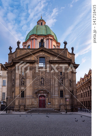 Historic Church of Saint Francis of Assisi with green Baroque dome in Prague City Czech Republic, showcasing ornate European architecture and a peaceful cobblestone square beneath a blue sky 141718435