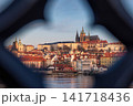 Prague Castle and Saint Vitus Cathedral framed through historic bridge architecture across the Vltava River, revealing iconic red rooftops and the timeless skyline of Prague City Czech Republic 141718436