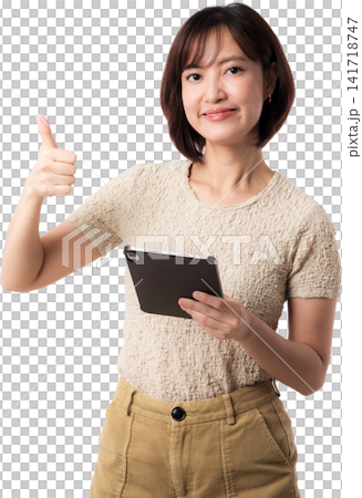 Asian woman tablet thumbs up portrait beige clothing showing cheerful expression against isolated background Asian woman tablet thumbs up portrait beige clothing showing cheerful expression against isolated background 141718747