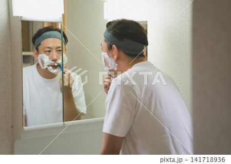洗面台の鏡に映る自分の顔を確認しながら髭を剃る40代男性のシェービング 洗面台の鏡に映る自分の顔を確認しながら髭を剃る40代男性のシェービング 141718936