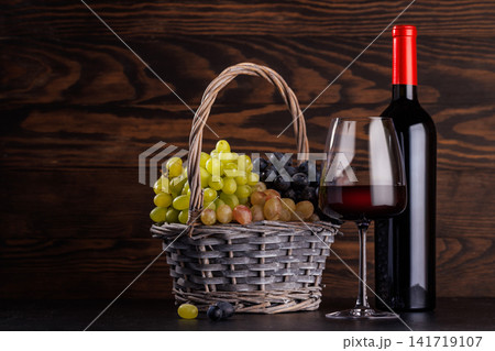 Red wine bottle with a glass and basket of fresh grapes 141719107