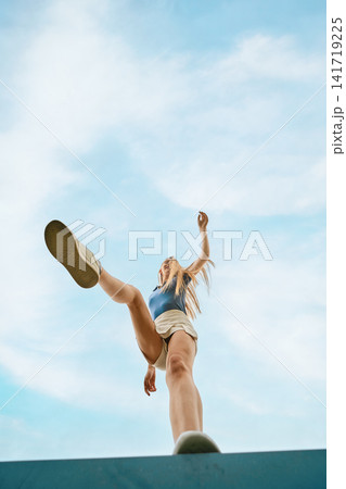 Funny woman performing high kick on blue background during bright sunny day outdoors Funny woman performing high kick on blue background during bright sunny day outdoors 141719225