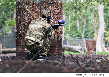 Paintball player with marker standing among old barrels in the forest 141719412