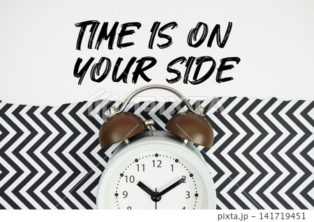 Time Is On Your Side text written on paper rip with alarm clock flat lay on black chevron background Time Is On Your Side text written on paper rip with alarm clock flat lay on black chevron background 141719451