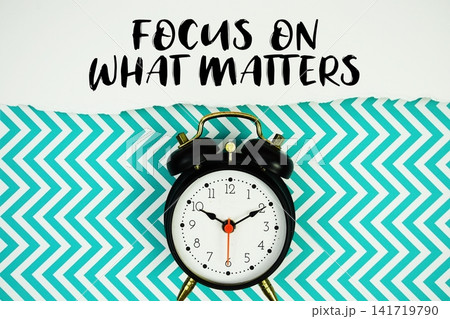 Focus on What Matters text written on paper with alarm clock on green chevron background Focus on What Matters text written on paper with alarm clock on green chevron background 141719790
