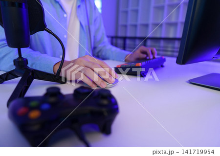 Gamer using computer mouse and keyboard at desk with controller for video gaming setup Gamer using computer mouse and keyboard at desk with controller for video gaming setup 141719954