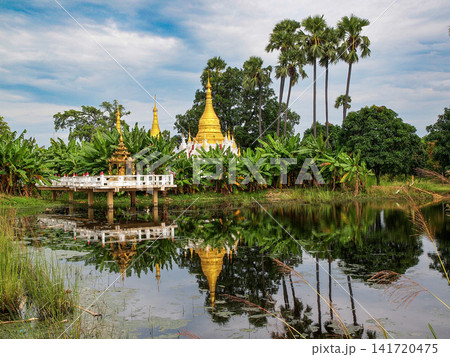 Golden pagoda and tropical lake reflections in Mandalay, Myanmar, with palm trees, lush greenery, and a peaceful temple landscape Golden pagoda and tropical lake reflections in Mandalay, Myanmar, with palm trees, lush greenery, and a peaceful temple landscape 141720475